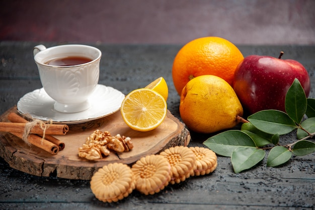 Xícara de chá com frutas e biscoitos na mesa escura de frente