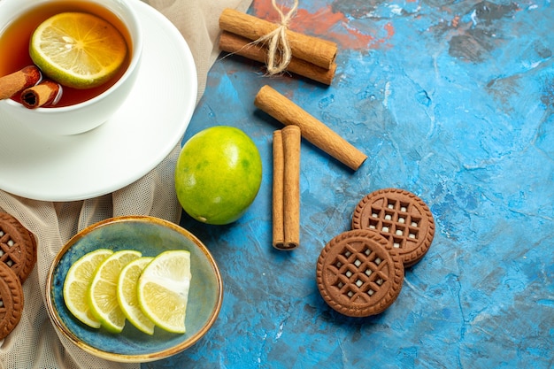 Xícara de chá com limão e canela, biscoitos xale bege e limão na mesa vermelha azul copiada