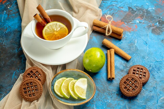 Xícara de chá com limão e canela, biscoitos xale bege e limão na mesa vermelha