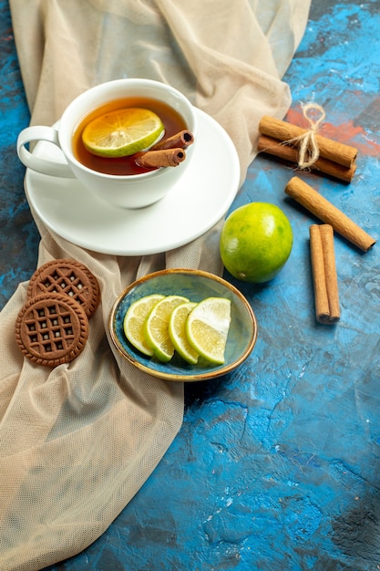 Xícara de chá com limão e canela, biscoitos xale bege e limão na superfície vermelha azul.