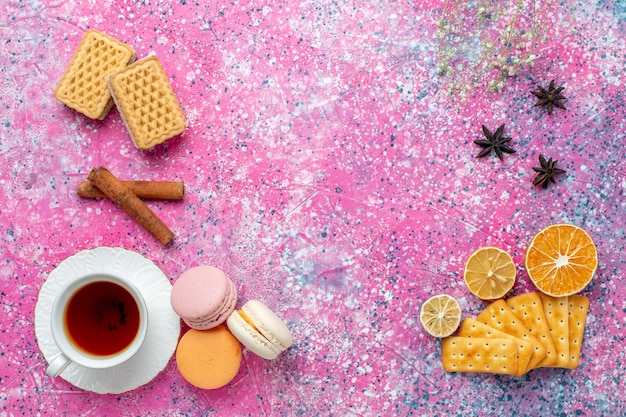 Xícara de chá com macarons franceses e biscoitos na mesa rosa claro com vista de cima