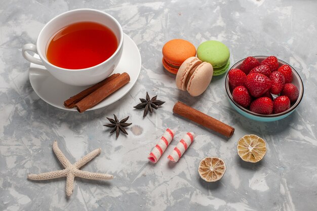 Xícara de chá com morangos frescos e macarons franceses na mesa branca com vista de cima