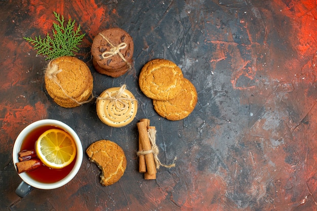 Xícara de chá de canela em pau de canela com biscoitos diferentes amarrados com corda na mesa vermelha escura