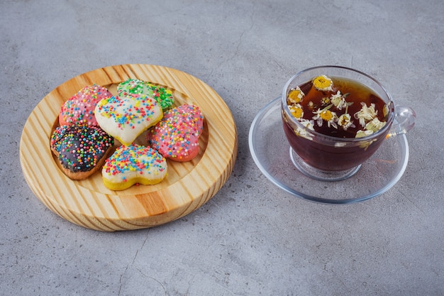 Xícara de chá de ervas com prato de biscoitos doces na superfície de pedra.