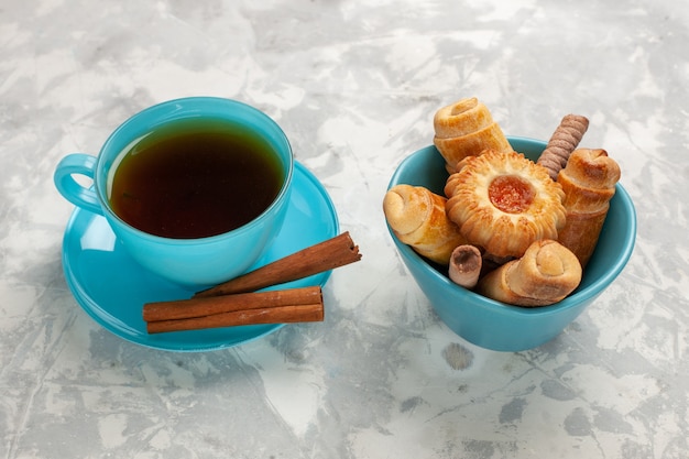 Xícara de chá de frente com biscoitos e rosquinhas no biscoito de torta de bolo de superfície branca