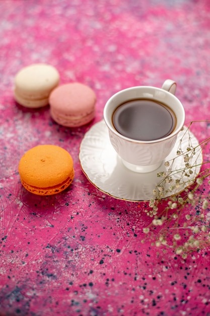Xícara de chá de frente para dentro da xícara no prato com macarons franceses na mesa rosa