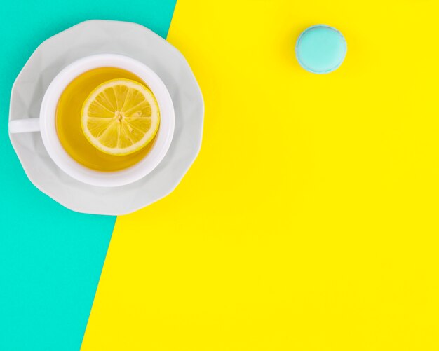 Xícara de chá de limão branco e Pires com macaroon no pano de fundo turquesa e amarelo