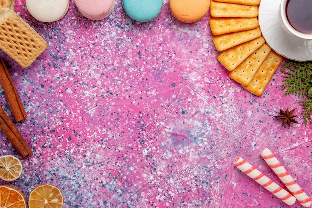 Foto grátis xícara de chá de vista de cima com biscoitos e macarons franceses na mesa rosa