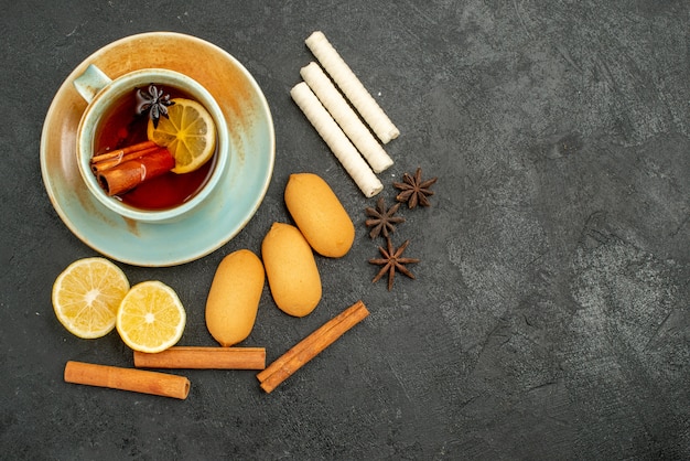 Xícara de chá de vista superior com limão e biscoitos no fundo escuro