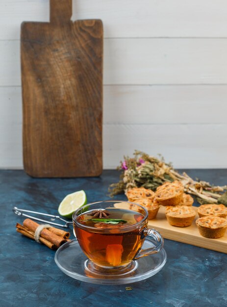 Xícara de chá e biscoitos com coador de biscoitos, flores, canela, limão e chá