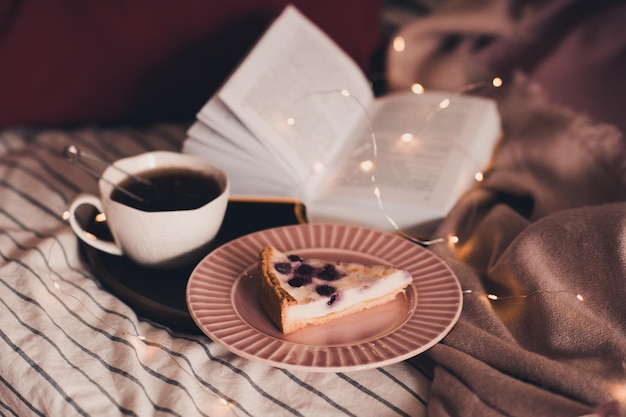 Xícara de chá preto, saboroso bolo de frutas e livro aberto com luzes brilhantes em close up da cama. bom dia. hora do café da manhã.