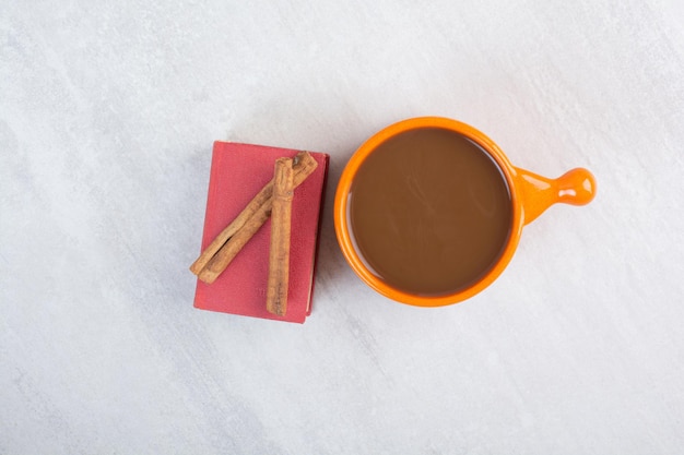 Xícara de chocolate quente, livro e canelas na superfície cinza