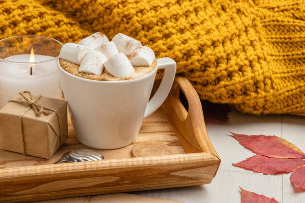 Xícara de marshmallows com presente e vela ao lado do suéter