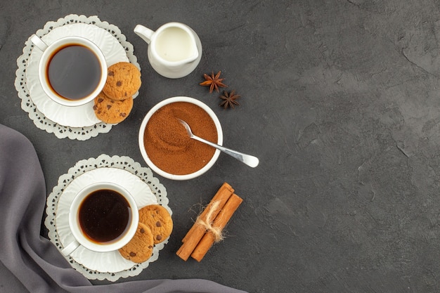 Xícaras de café canela biscoitos xícara de leite cacau em pó em uma tigela na superfície escura