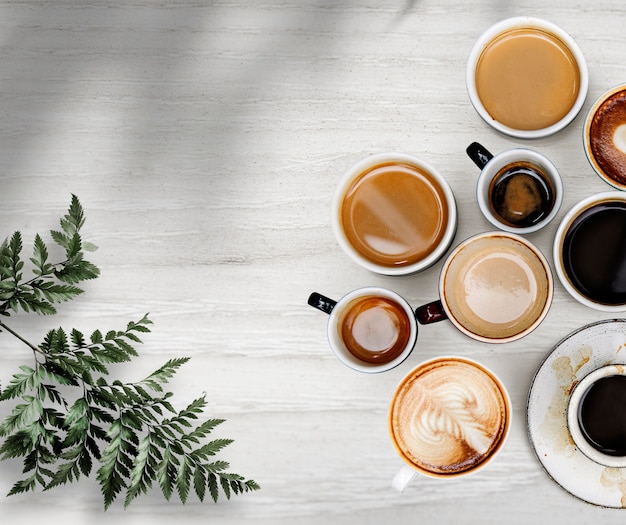 Xícaras de café misturadas com uma folha em um papel de parede branco texturizado de madeira