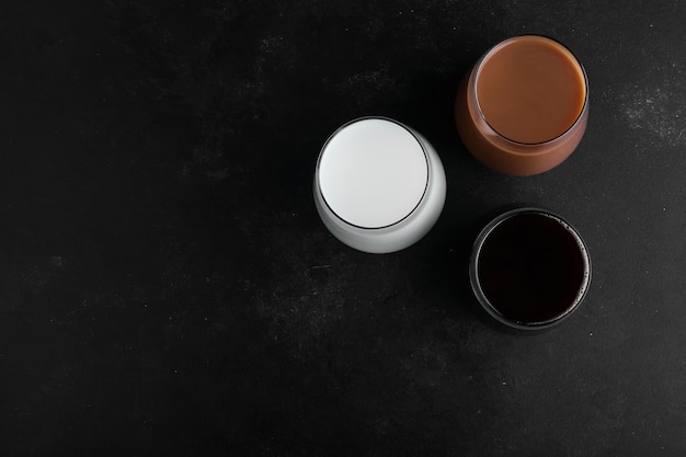 Xícaras de leite, chocolate e café expresso escuro na superfície preta, vista superior.