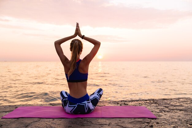 Yoga ao nascer do sol. mulher esportiva, praticando ioga, sentado no cais em posição de lótus