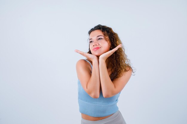 Foto grátis yong girl está olhando para longe segurando a mão sob o queixo no fundo branco