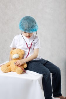 6-jähriger junge in medizinischem einweghut untersucht plüsch-teddybär