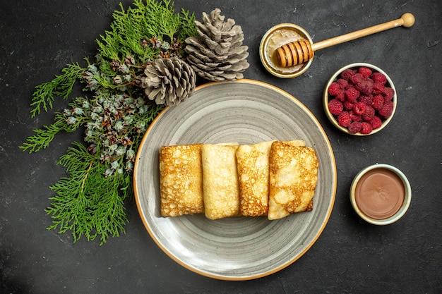 Abendessenhintergrund mit köstlichem Pfannkuchenhonig und Schokoladenhimbeer- und Nadelbaumkegel auf schwarzem Hintergrund