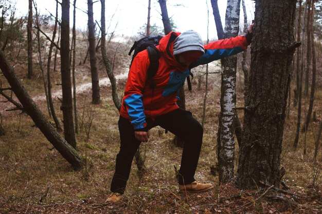 Abgenutzter Wanderer, der im Wald steht und sich auf den Stamm stützt