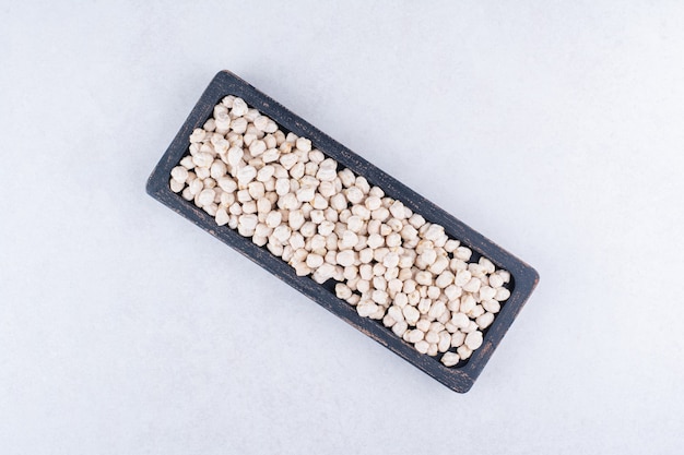 Abgenutztes Tablett gefüllt mit einer Portion roher Kichererbsen auf Marmoroberfläche