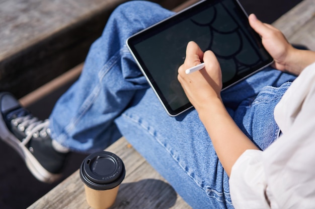 Kostenloses Foto abgeschnittene aufnahme weiblicher hände, die auf einem digitalen grafiktablett mit stift zeichnen, sitzend bei einer tasse kaffee o