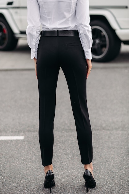 Abgeschnittenes Foto einer nicht wiederzuerkennenden Frau in weißem Hemd und formeller schwarzer gerader Hose und schwarzen Lederabsätzen, die auf der Straße stehen. Mode-Modell. Dresscode-Konzept.