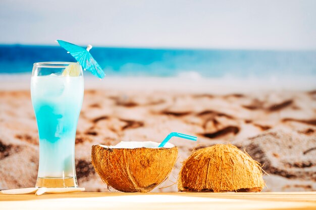 Abkühlendes blaues Cocktail und Kokosnussmilch auf sandigem Strand