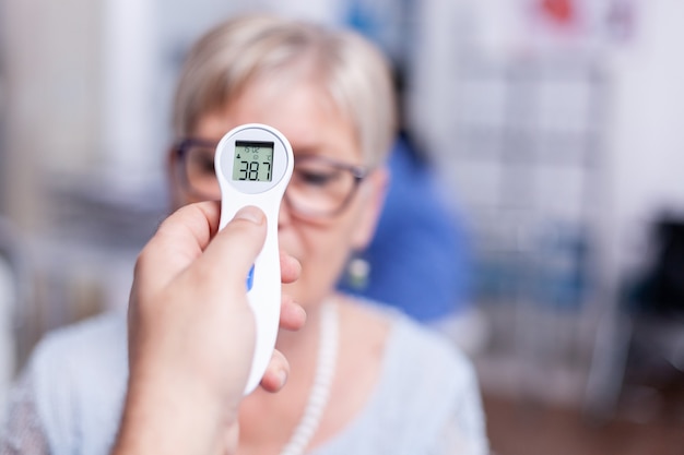 Ablesen der Körpertemperatur mit Infrarot-Thermometer während der ärztlichen Untersuchung