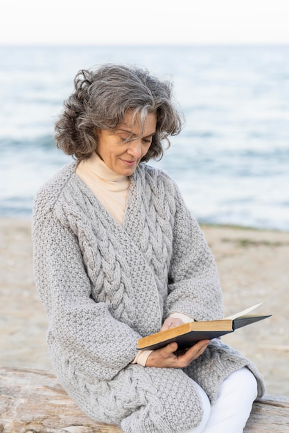 Kostenloses Foto Ältere frau am strand, die ein buch liest