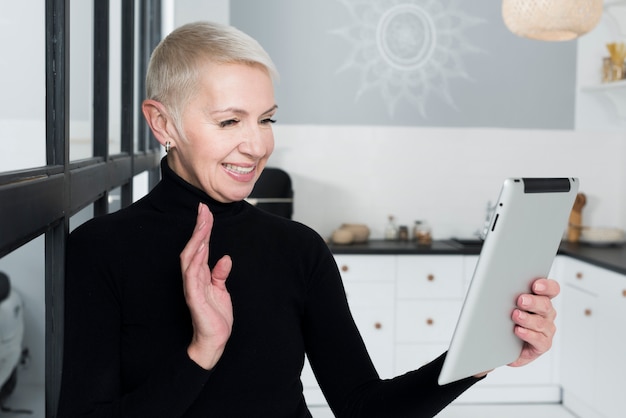 Kostenloses Foto Ältere frau des smiley in der küche, die an der tablette wellenartig bewegt