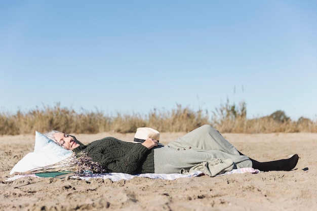 Kostenloses Foto Ältere frau, die auf sand liegt