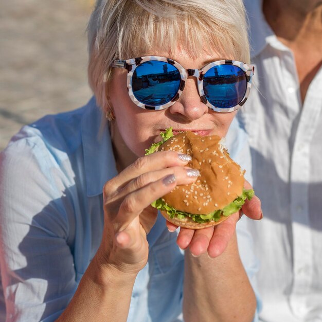 Ältere Frau, die einen Burger am Strand verschlingt