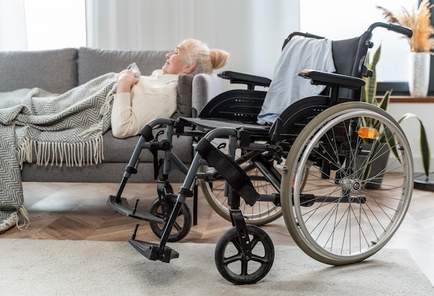 Ältere Frau, die im Bett neben einem Rollstuhl liegt