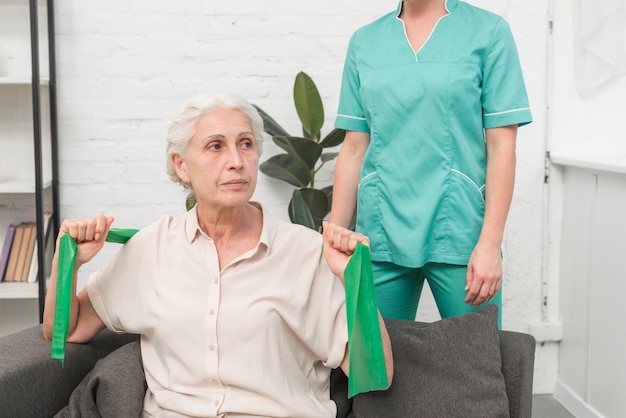 Kostenloses Foto Ältere frau, die mit dem grünen ausdehnungsband sitzt vor weiblicher krankenschwester trainiert