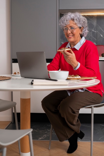 Kostenloses Foto Ältere frau, die zu hause feigen isst und laptop benutzt
