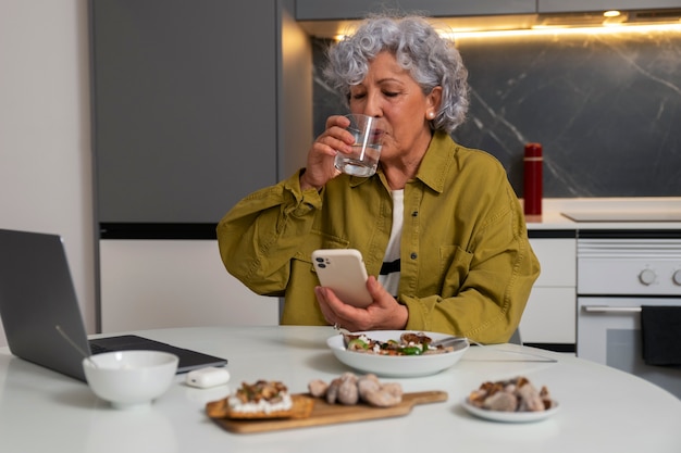 Kostenloses Foto Ältere frau, die zu hause feigen isst und smartphone benutzt