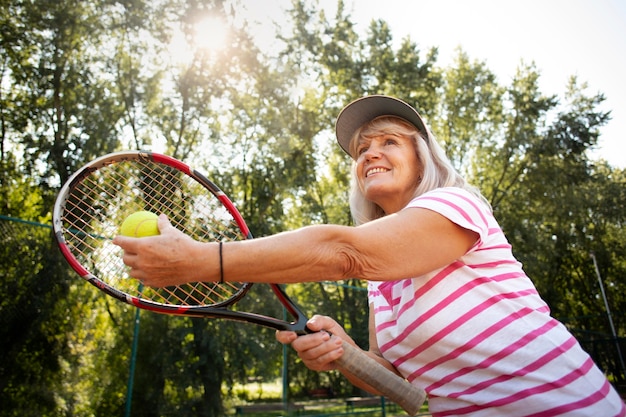 Ältere frau mit mittlerem schuss, die tennis spielt