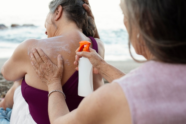 Kostenloses Foto Ältere frauen, die sonnencreme auf der rückseite am strand auftragen