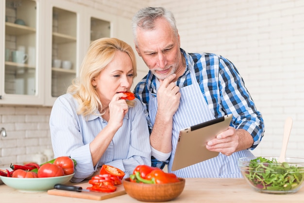 Ältere Paare, die digitale Tablette beim Zubereiten des Lebensmittels in der Küche betrachten