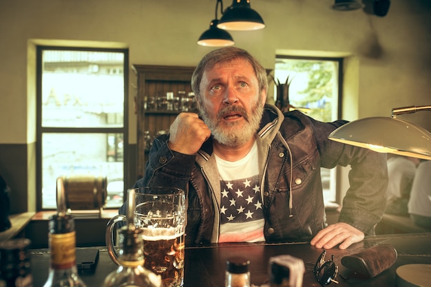 älterer bärtiger Mann, der Bier in der Kneipe trinkt