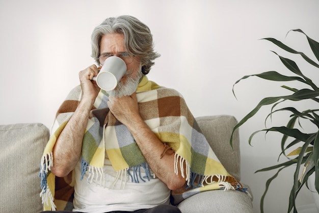 Älterer mann, der allein auf sofa sitzt. kranker mann mit plaid bedeckt. großvater mit einer tasse tee.