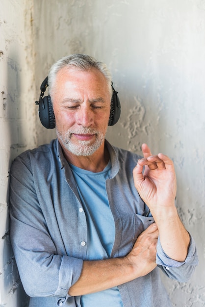 Kostenloses Foto Älterer mann, der auf hörender musik der wand auf kopfhörer sich lehnt