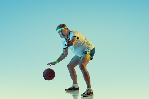 Kostenloses Foto Älterer mann, der basketball auf gradientenwand im neonlicht spielt