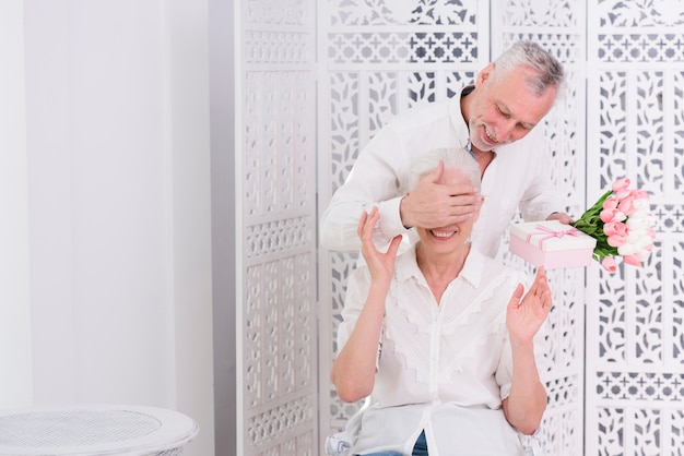 Kostenlose Foto Alterer Mann Der Die Augen Seiner Frau Mit Einer Hand Bedeckt Und Ihr Ein Geschenk Gibt