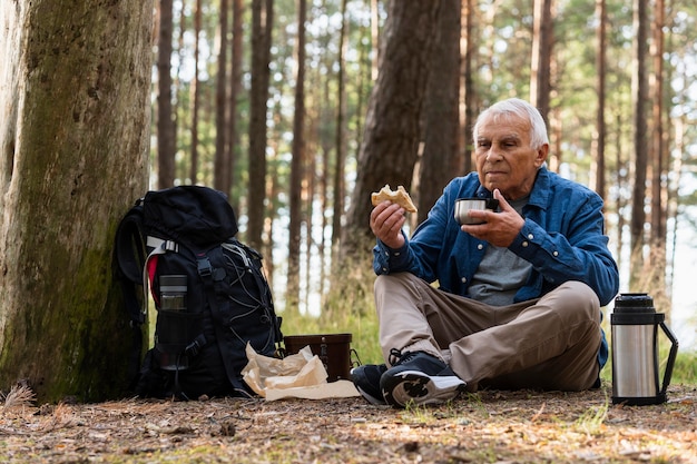 Kostenloses Foto Älterer mann, der ein getränk beim rucksackwandern in der natur hat