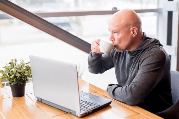 Kostenloses Foto Älterer mann, der einen kaffee trinkt, während den laptop benutzt