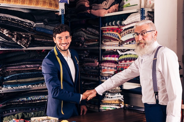 Kostenloses Foto Älterer mann, der hand mit lächelndem jungem männlichem schneider in seinem shop rüttelt