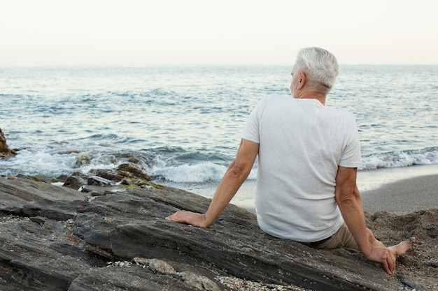 Älterer Mann, der sich am Strand ausruht und das Meer bewundert